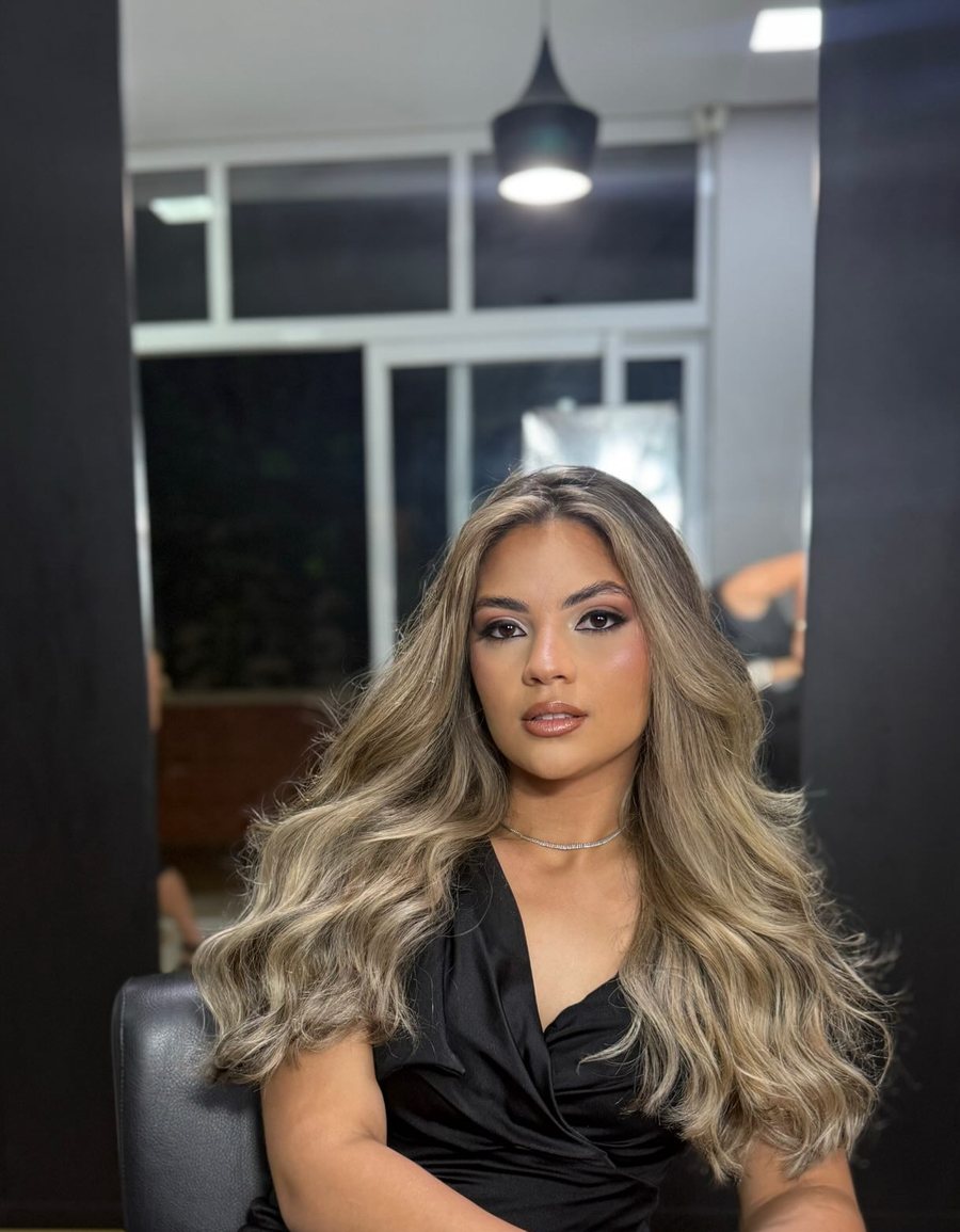Cliente com loiro iluminado e fios ondulados, sentada na poltrona do salão